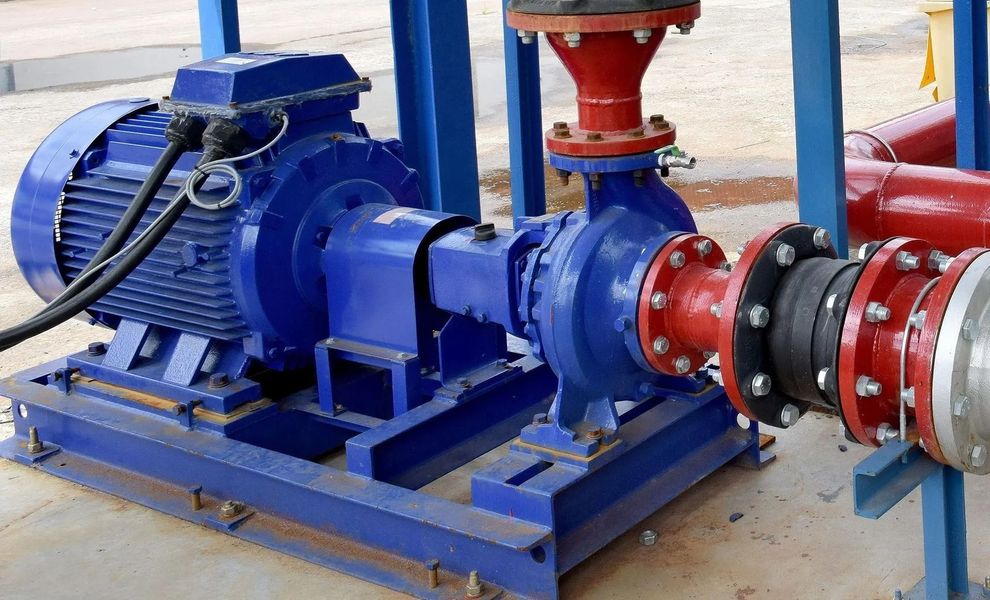 Blue industrial pump connected to red pipes on a metal skid in a factory setting