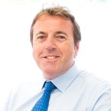 A man in a blue shirt and blue tie is smiling for the camera.