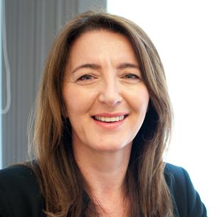 A woman with long brown hair is smiling and wearing a black jacket.