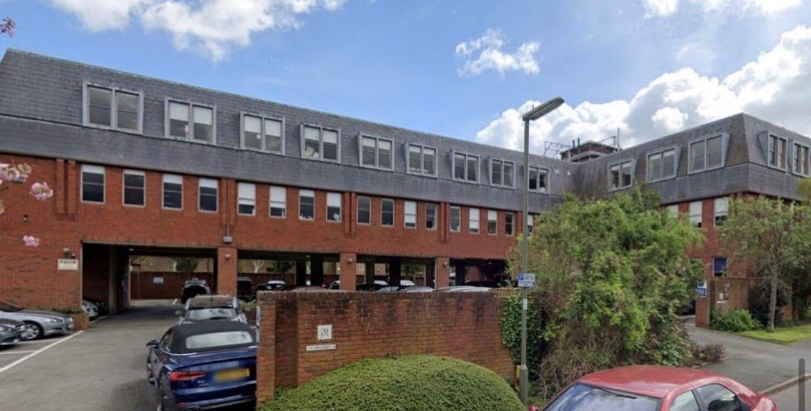 Brick building with multiple floors, various windows, and a car park on a cloudy day.