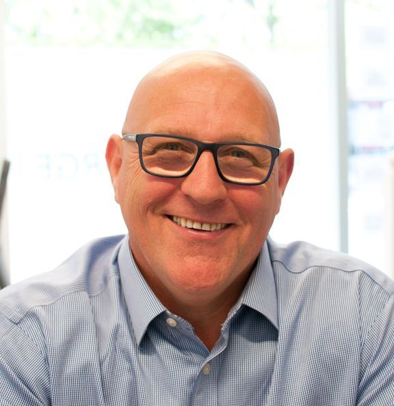 A bald man wearing glasses and a blue shirt smiles for the camera