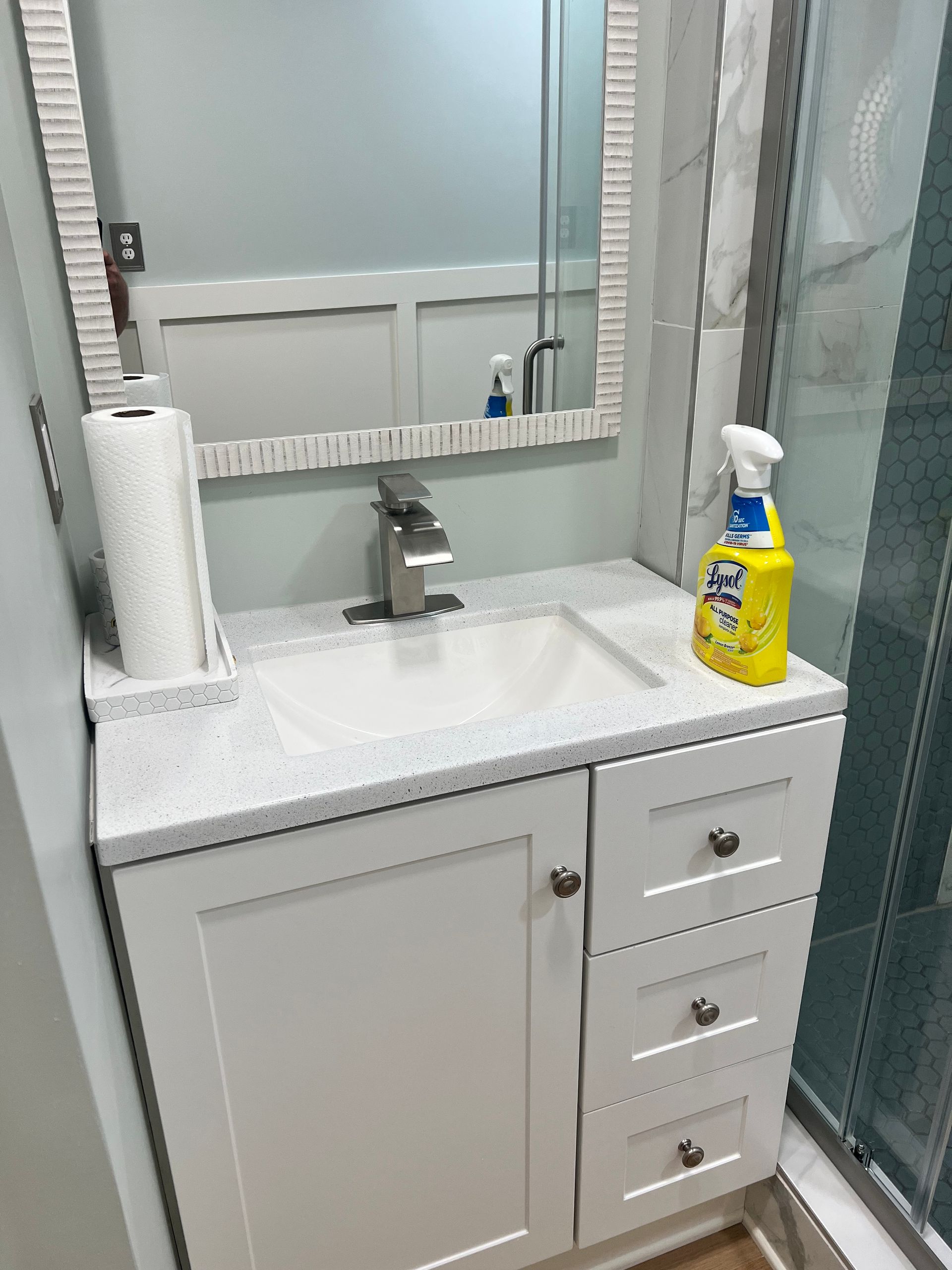 Small white bathroom vanity with sink, mirror, and cleaning supplies.