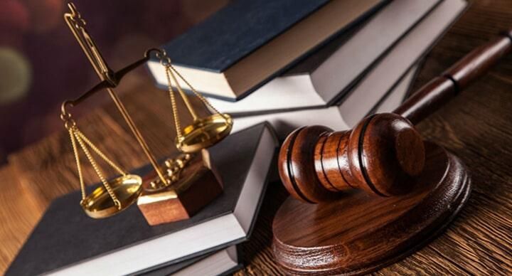 El mazo de un juez está sobre una mesa de madera al lado de una pila de libros y una balanza de la justicia.