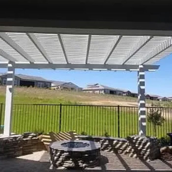 A pergola over a patio with a table and chairs and a fire pit. A pergola over a patio with a table and chairs and a fire pit.