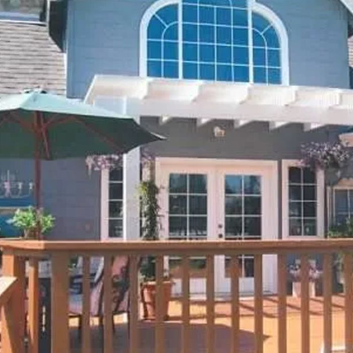 A patio with a pergola and a table and chairs A large house with a deck and umbrellas in front of it.