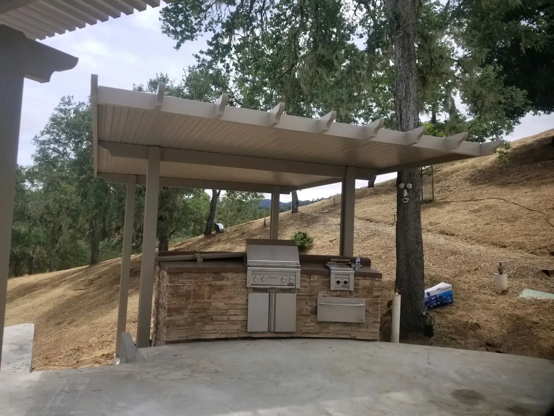 An outdoor kitchen with a grill under a pergola