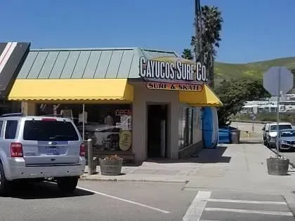 A car is parked in front of a building that says calico 's surf co.
