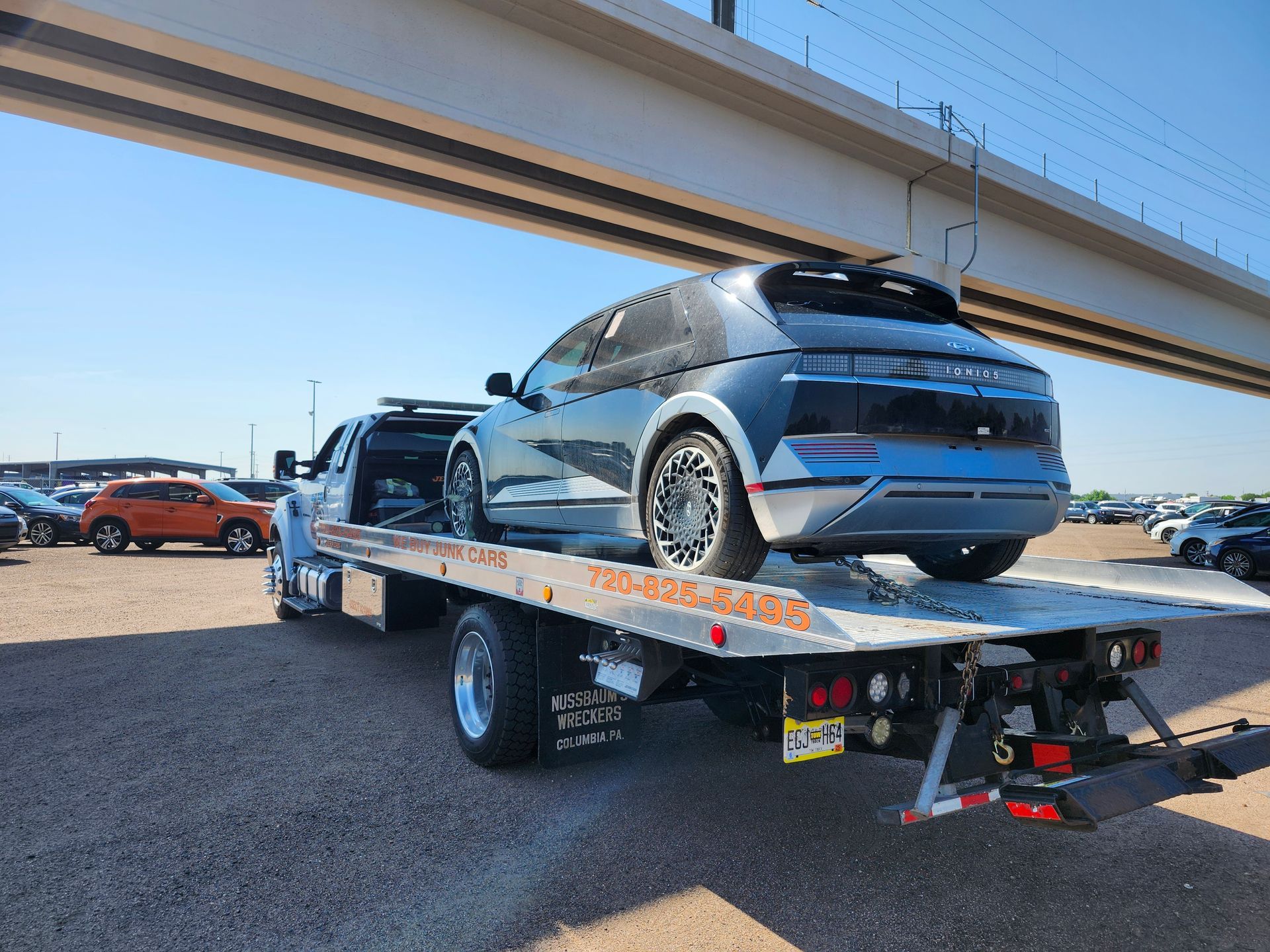 A silver Hyundai Ioniq 5 being transported on a flatbed tow truck beneath a concrete overpass.