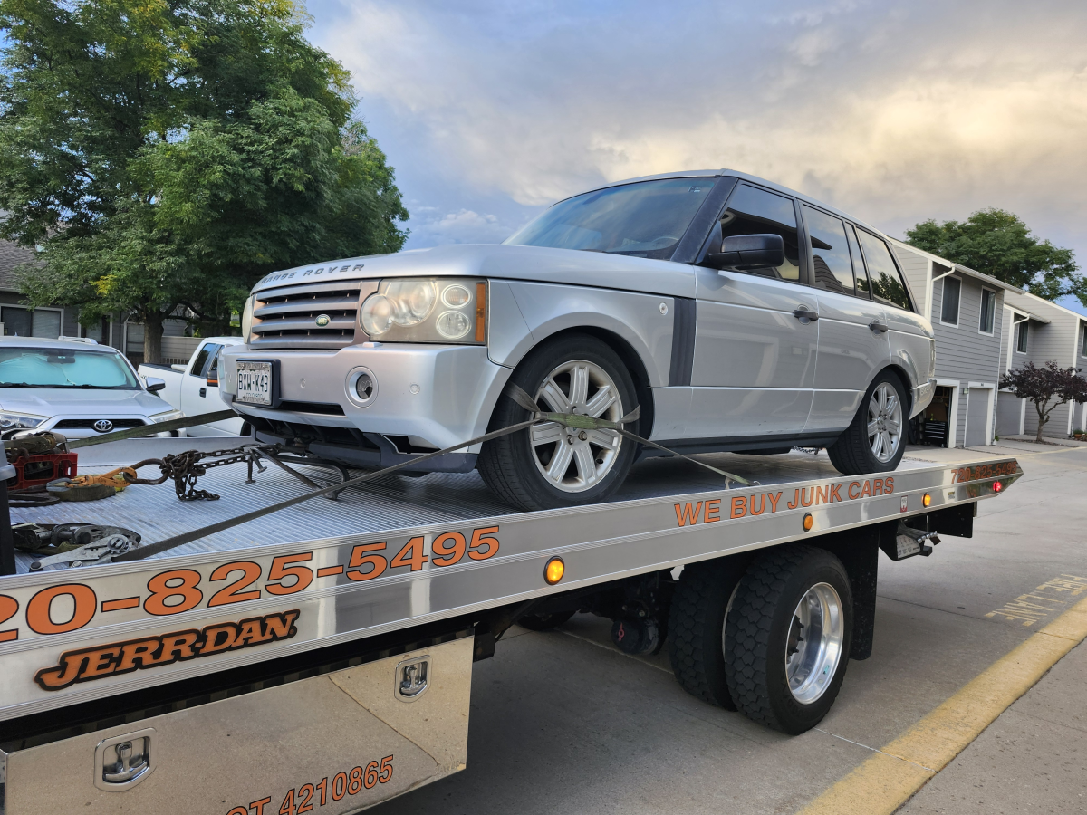 A silver Range Rover SUV is secured on the bed of a Jerr-Dan flatbed tow truck parked on a residential street.