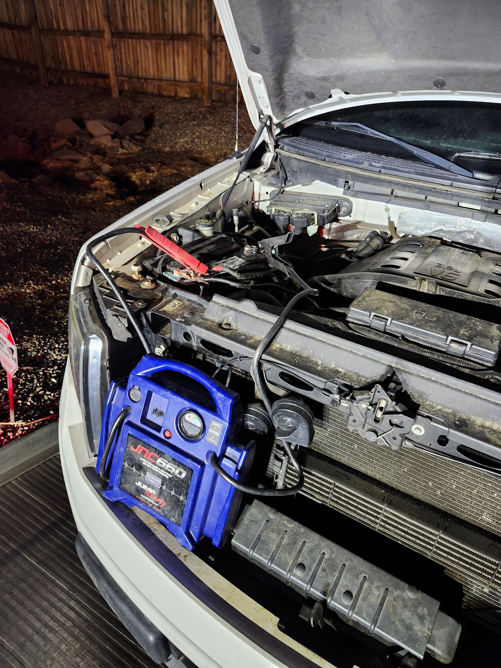 A blue portable jump starter connected to a vehicle's battery in an open engine bay at night.