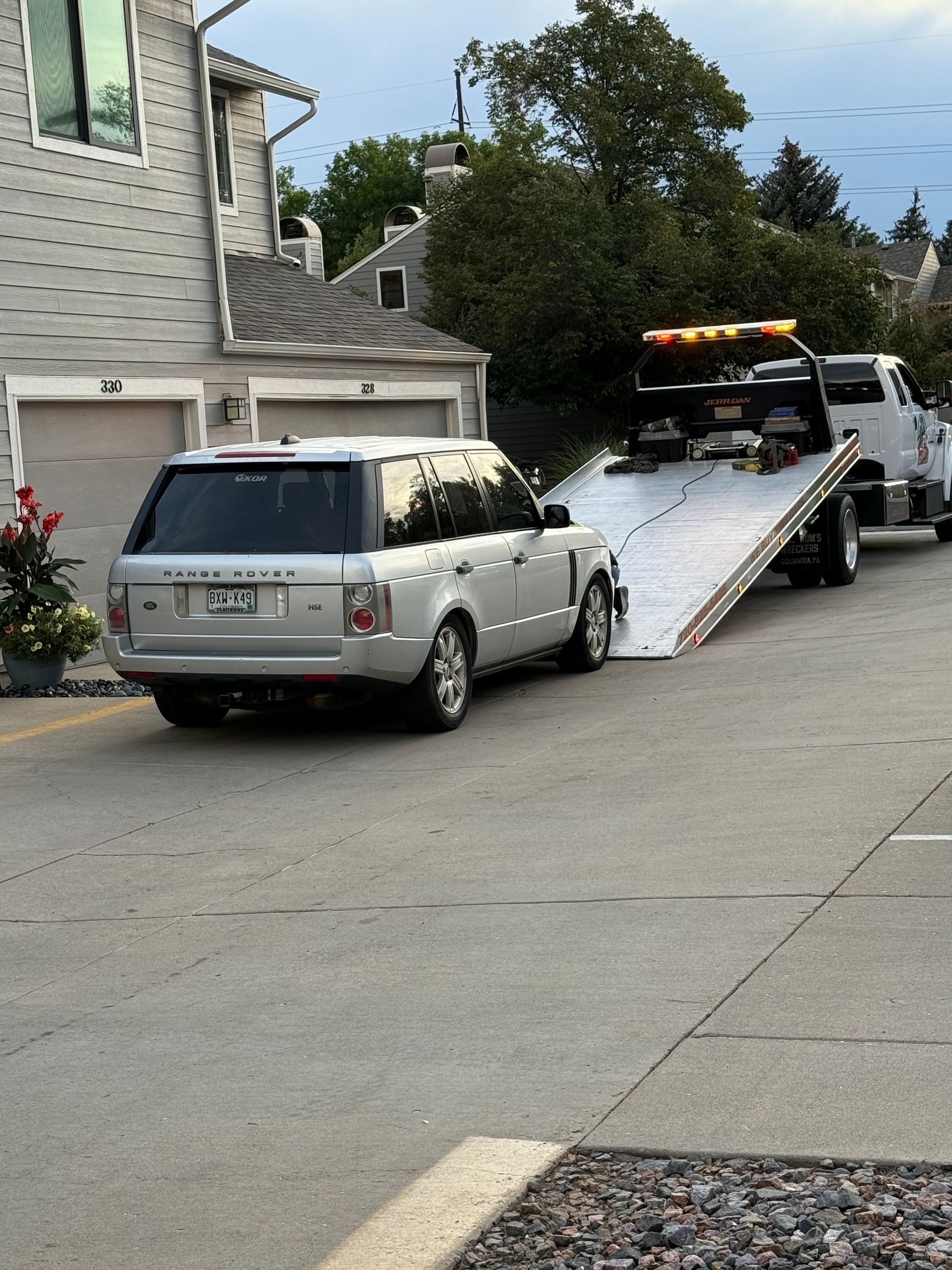 A silver SUV being loaded onto a flatbed tow truck on a residential street.