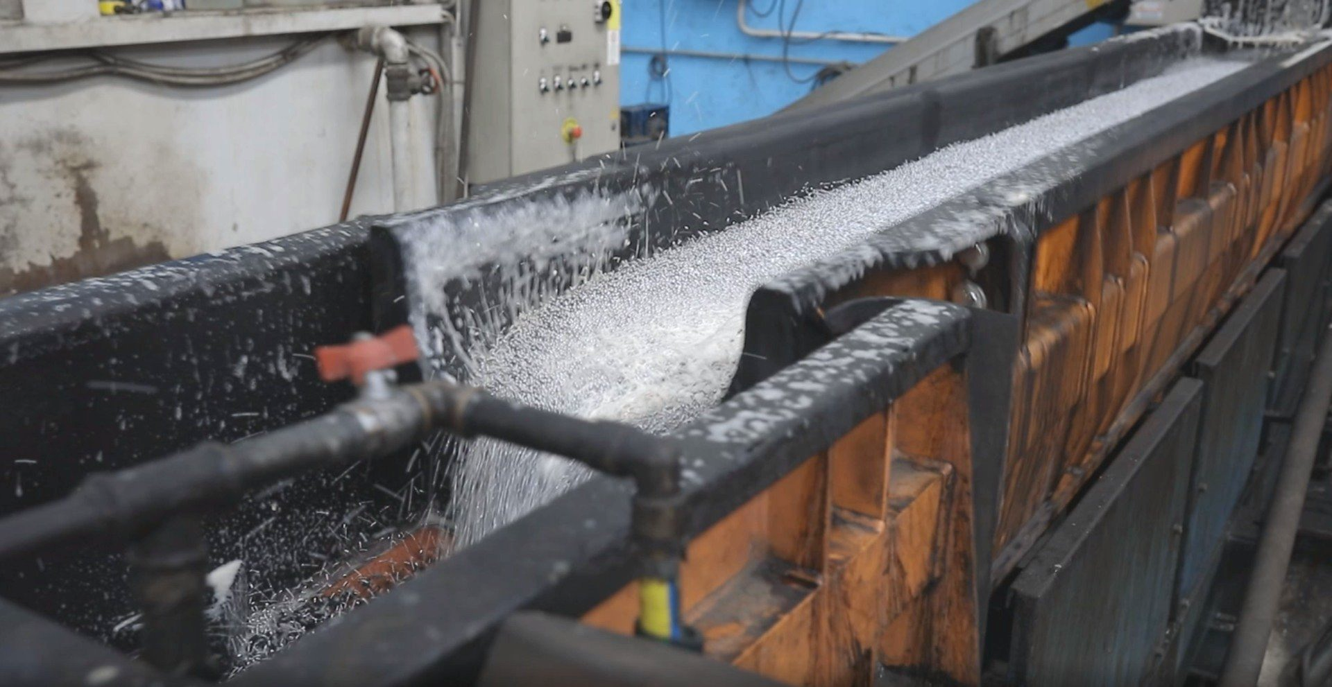 Trucioli metallici che scorrono lungo una vasca industriale, probabilmente destinati al riciclaggio o alla lavorazione.