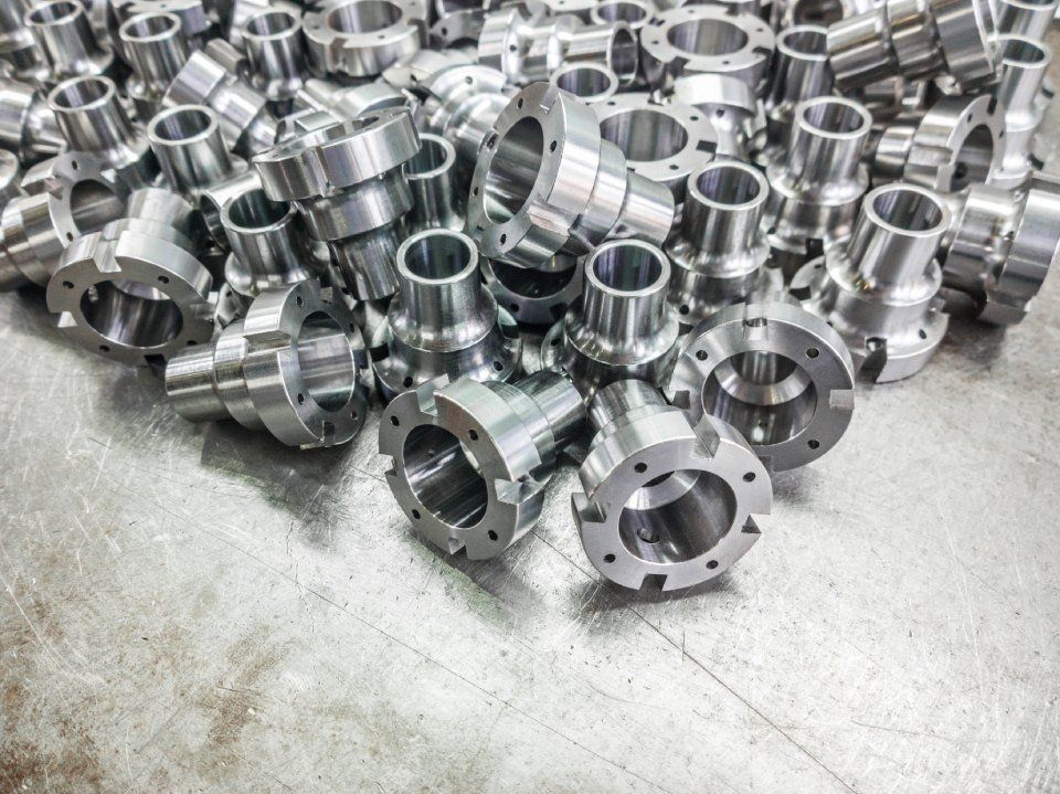 Mucchio di parti metalliche lucide e lavorate, di forma cilindrica e flangiata, su una superficie metallica.