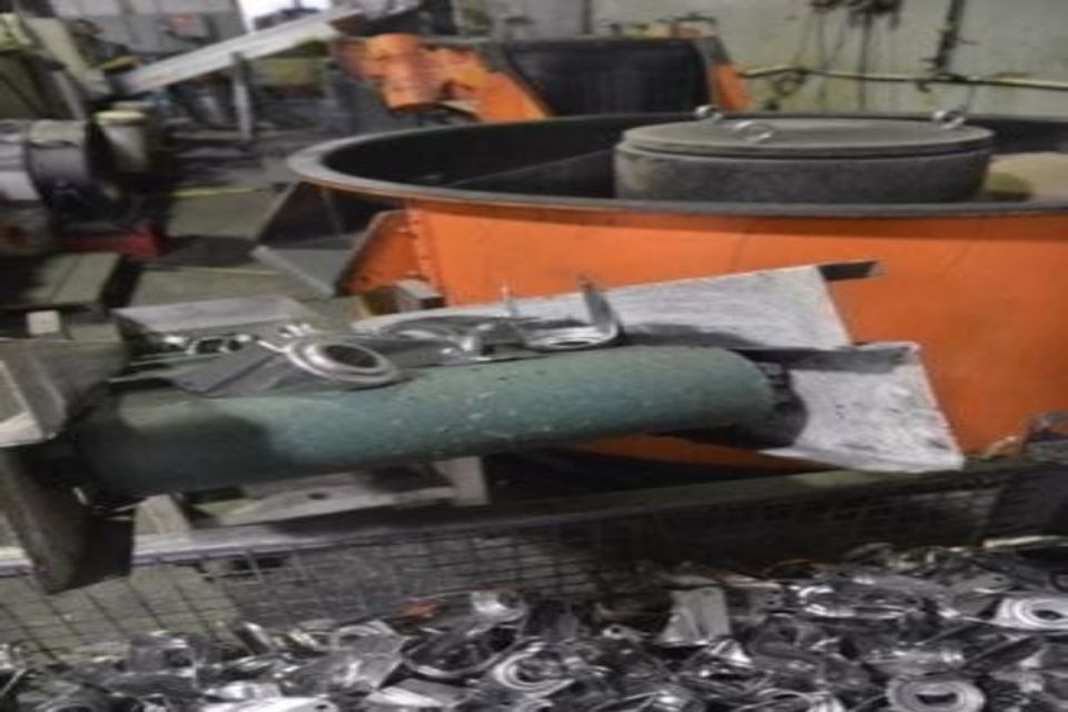 Rottami metallici e parti vicino a una macchina industriale arancione, in un ambiente di fabbrica.