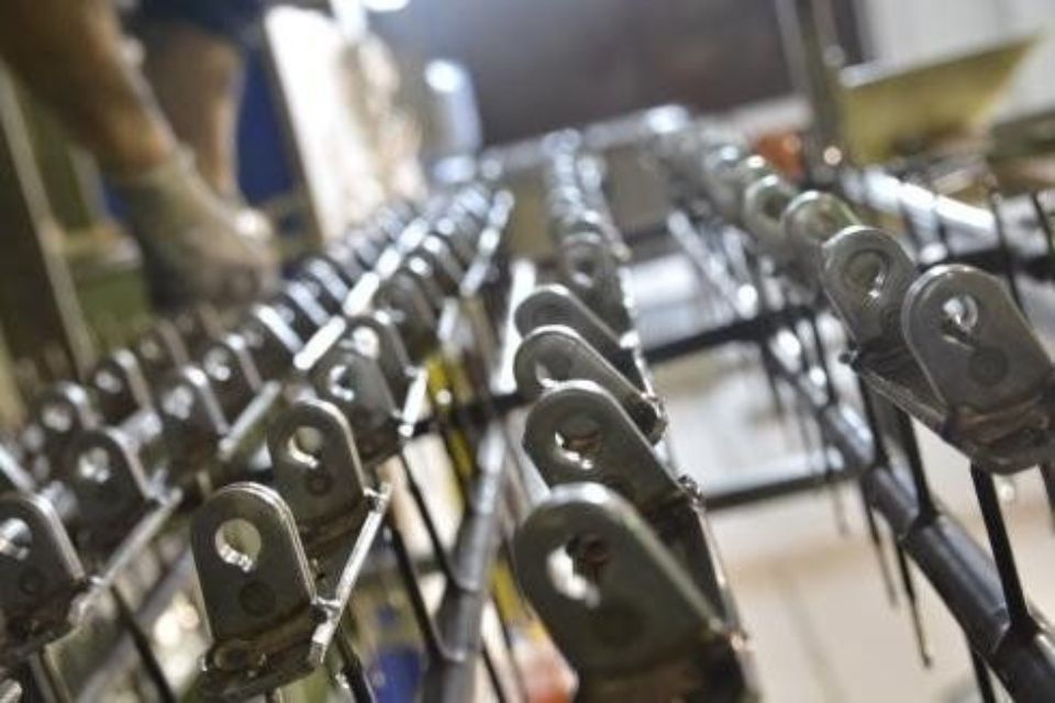 Componenti metallici appesi su rastrelliere, probabilmente destinati alla lavorazione industriale, con una persona sullo sfondo.