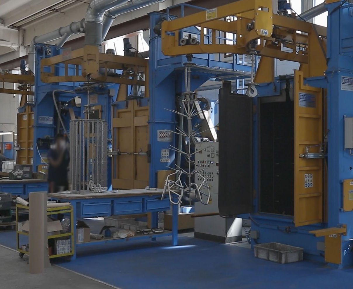 Macchina industriale blu e gialla in una fabbrica, con parti metalliche. È visibile una persona.