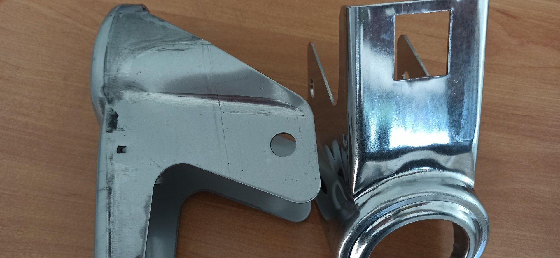 Due parti metalliche cromate, probabilmente di una macchina o di un elettrodomestico, poggiano su una superficie di legno.