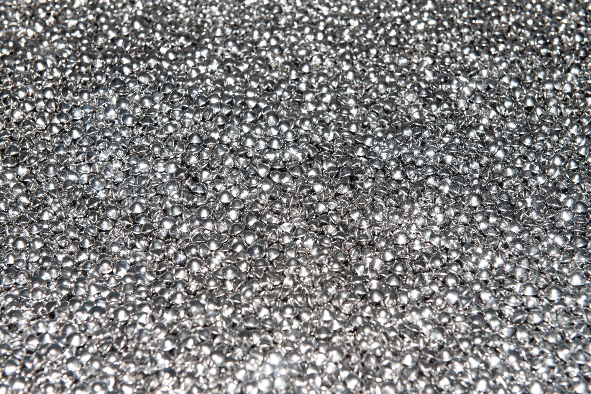 Mucchio di minuscoli strass argentati lucidi che riflettono la luce.