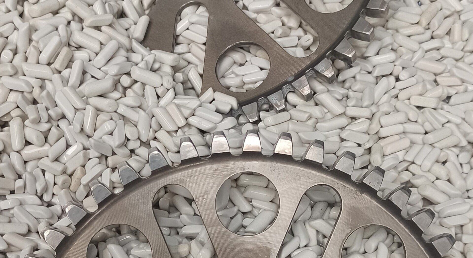 Due ingranaggi metallici sopra un letto di piccole palline bianche e cilindriche.