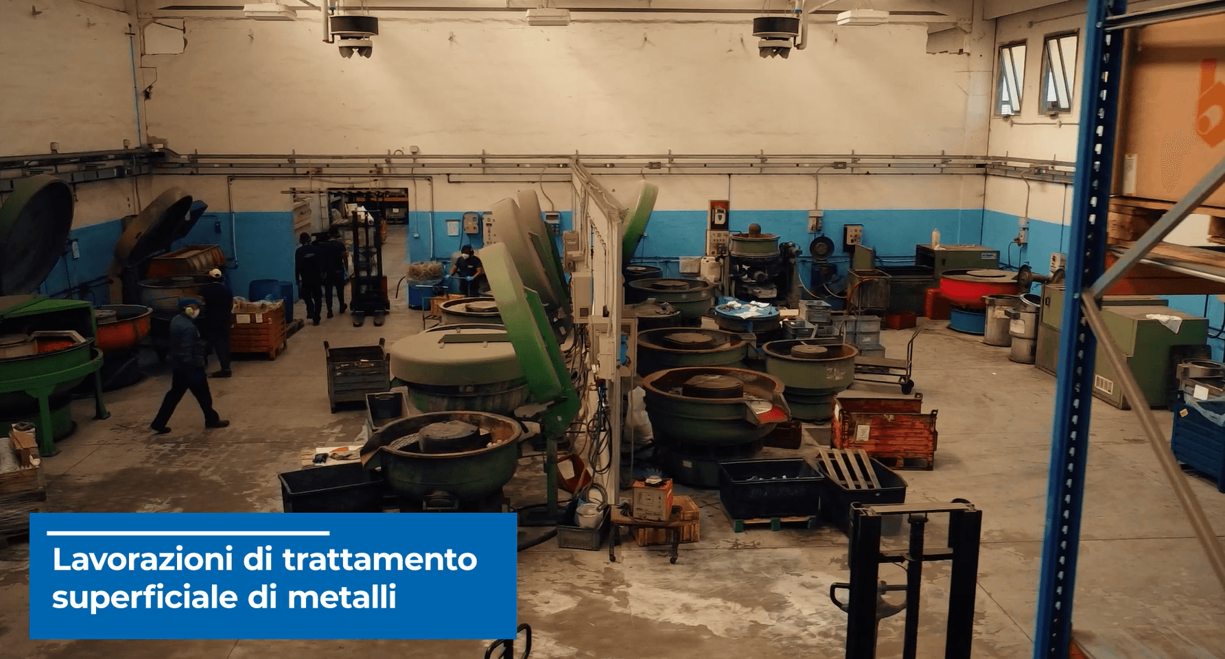 Interno dell'officina con macchinari per la lavorazione dei metalli, pareti blu e bianche e operai.