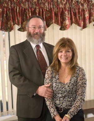 A man and woman are posing for a picture in front of a window.