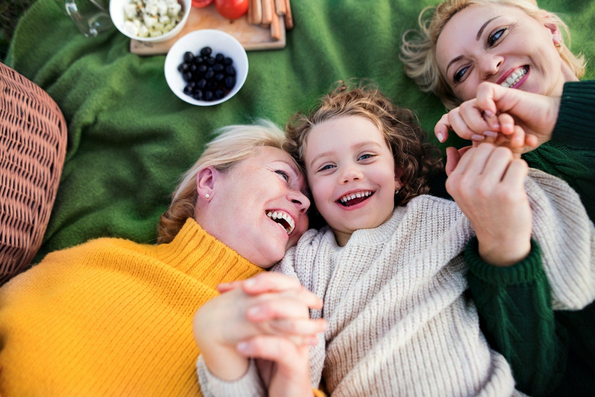 Three women and a child are laying on a blanket and laughing.
