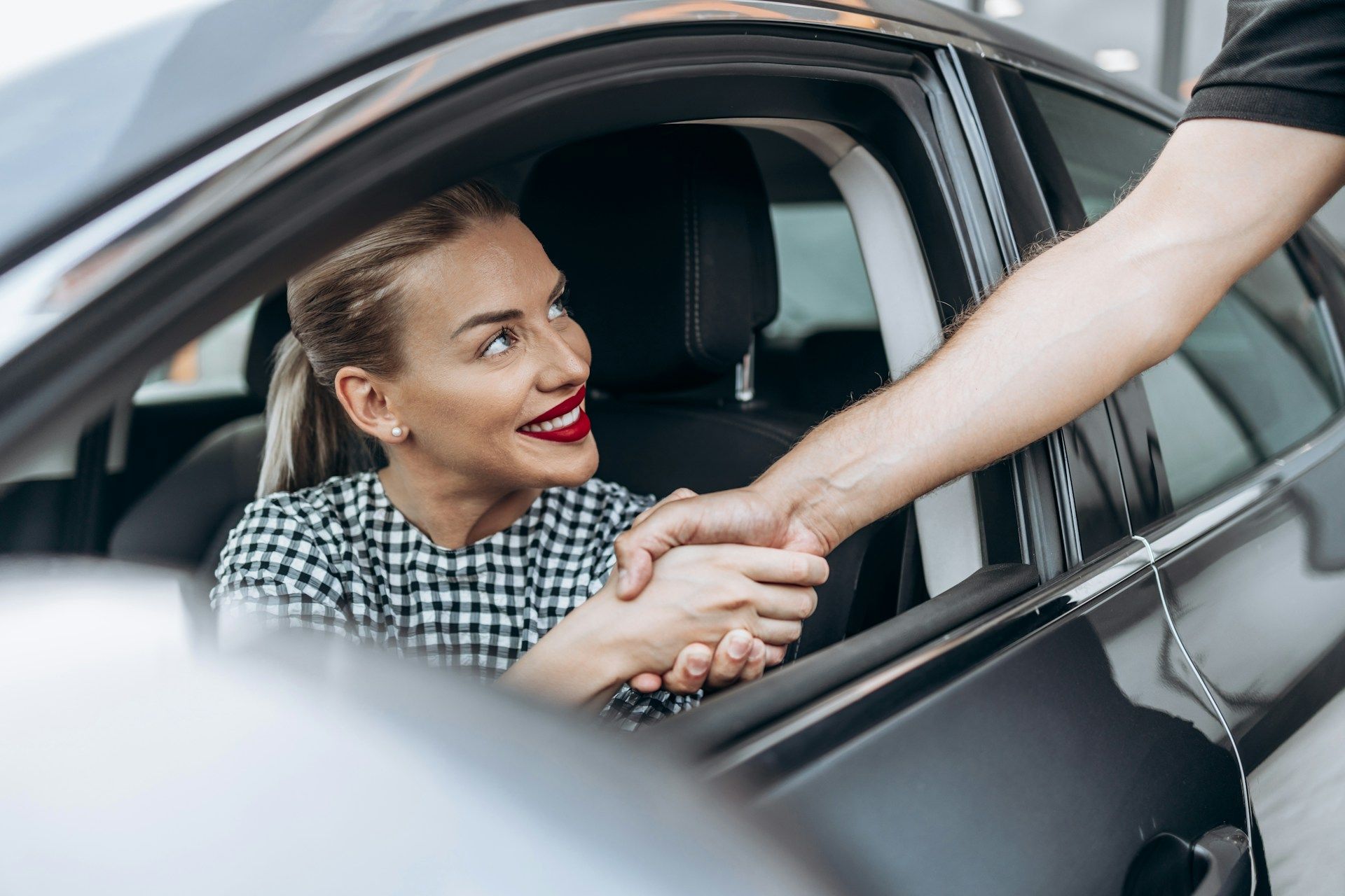 A woman is shaking hands with a man in a car.