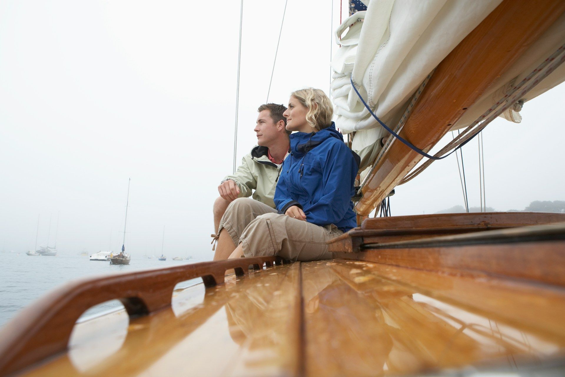A man and a woman are sitting on the deck of a sailboat looking out over the water.