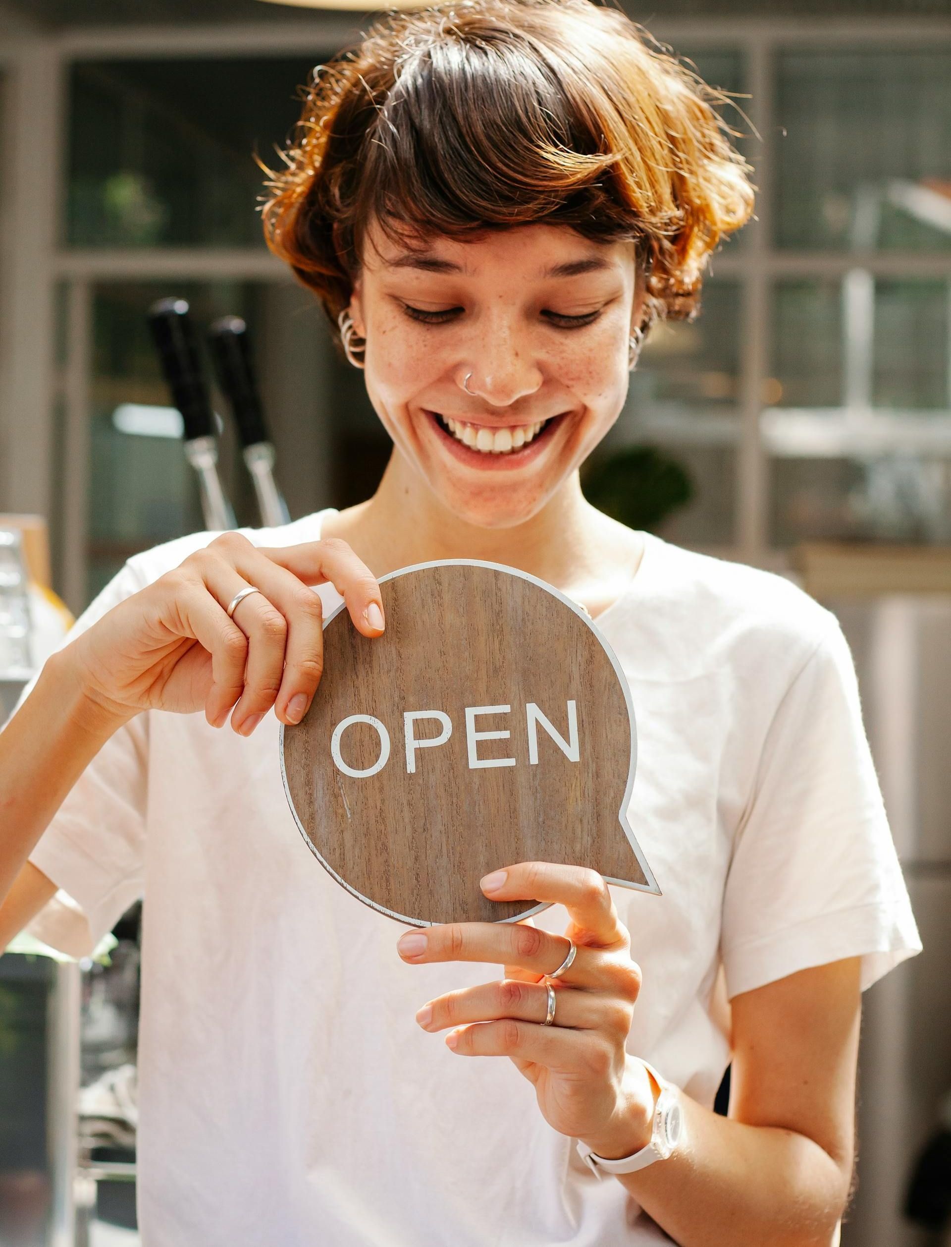 A woman is holding a wooden sign that says open.
