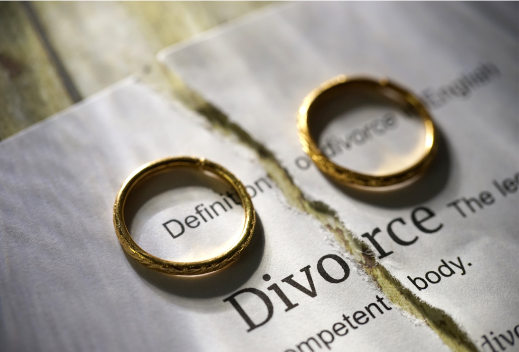 Two gold wedding rings sit on a torn paper that reads “Divorce.”