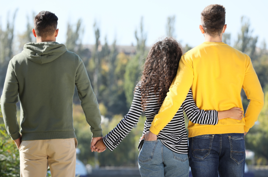 A person in striped shirt held between two others, one with arm around them, other holding their hand.