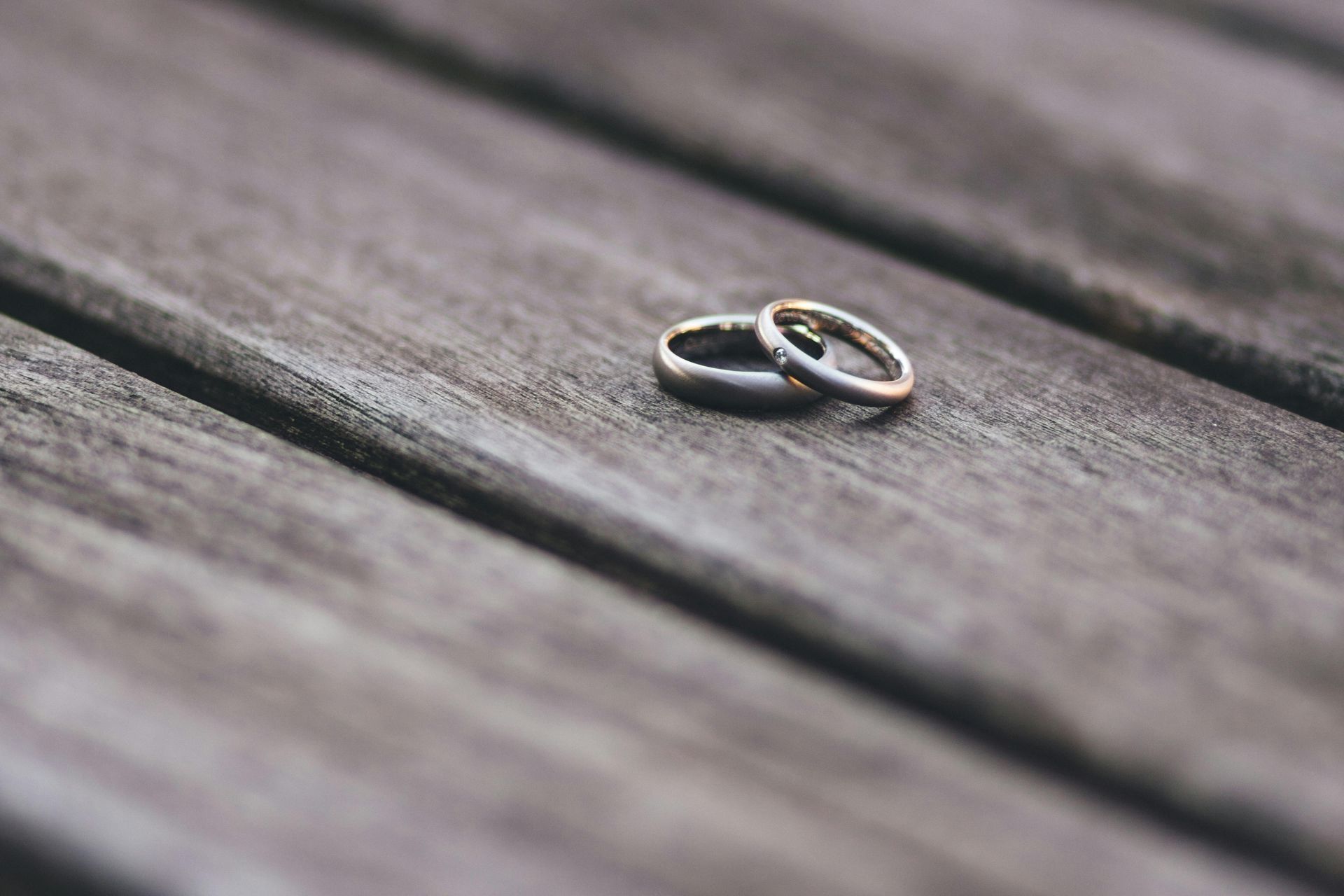 Two wedding rings on a weathered wooden surface, one slightly behind the other.