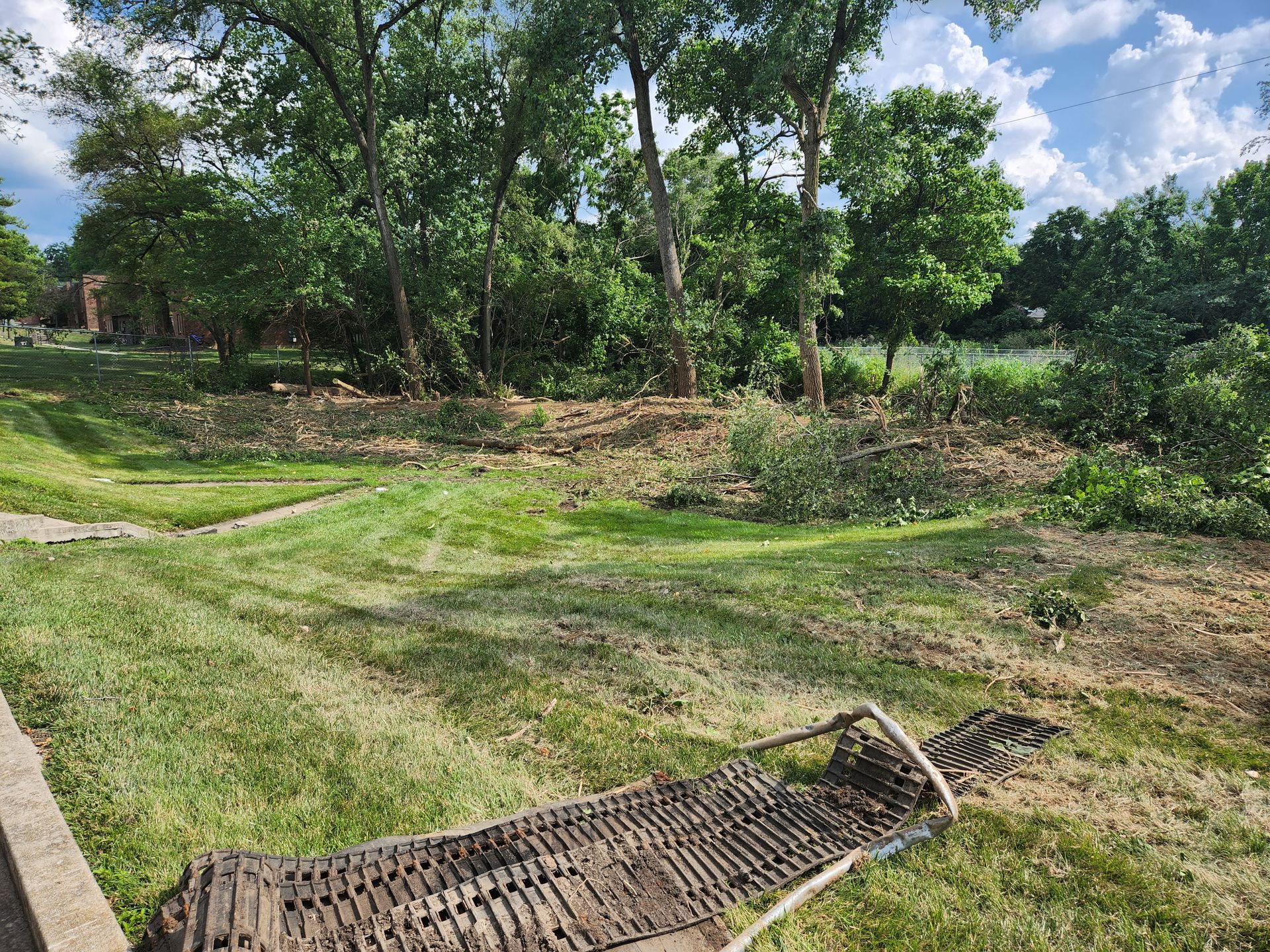 A field with freshly mowed grass, some cleared debris, and a collapsed metal lawn chair in the foreground.