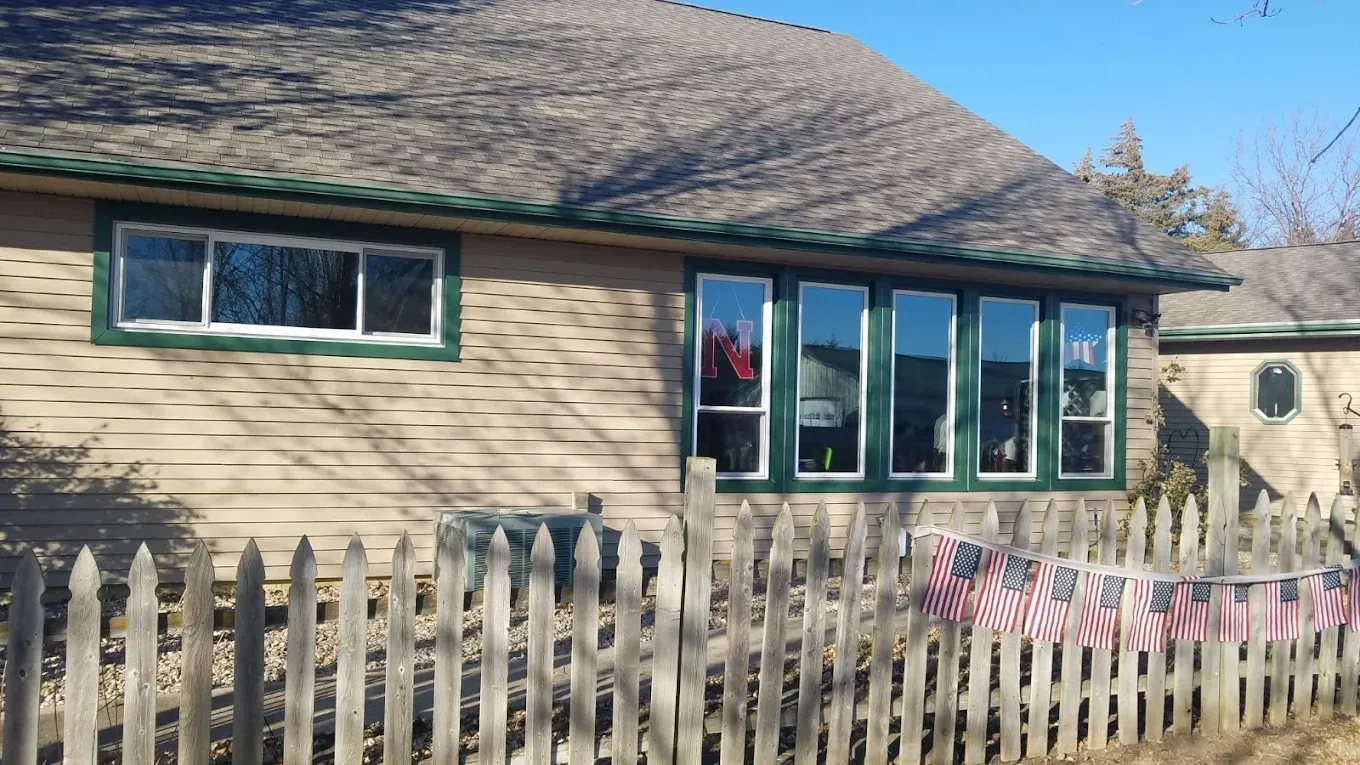 Tan house with green trim and multiple windows, a wooden fence with American flags.