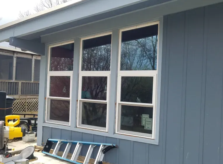 Three new windows installed on a blue house exterior, with a ladder leaning below.