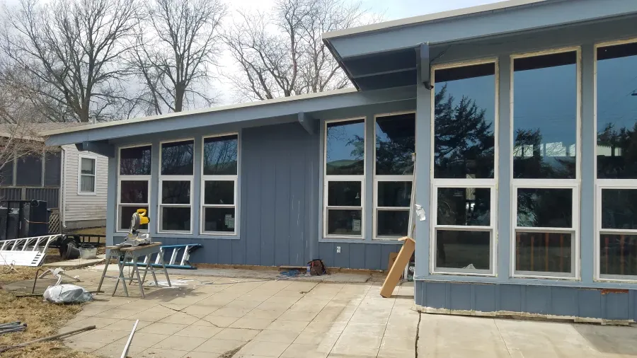 Blue house with many large windows, pale concrete patio, and outdoor furniture.