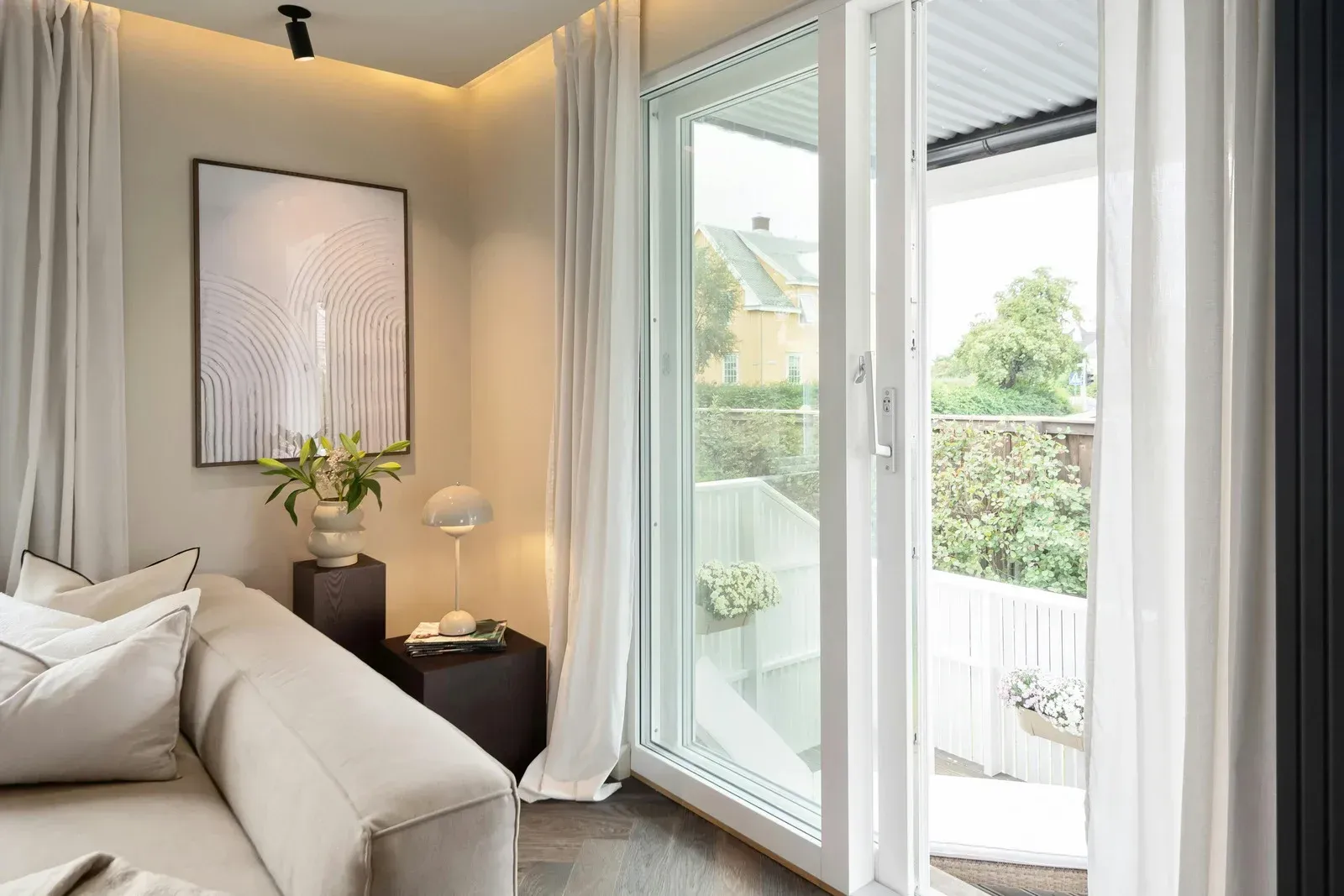 Cozy living room with sliding glass door to an outdoor area. Beige sofa, artwork, and white curtains.