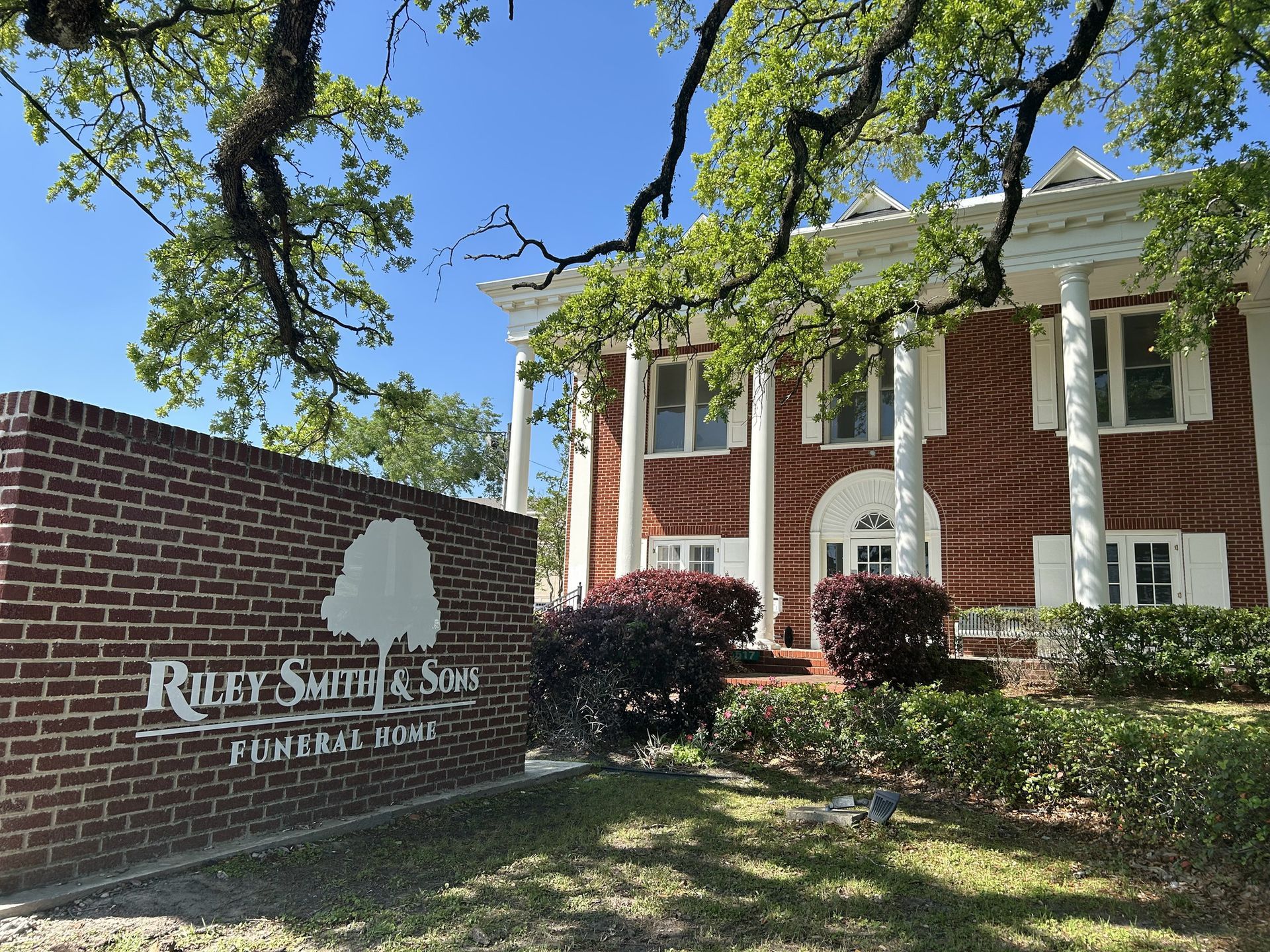 Brick sign and red-brick building with white columns at a sunny entrance.