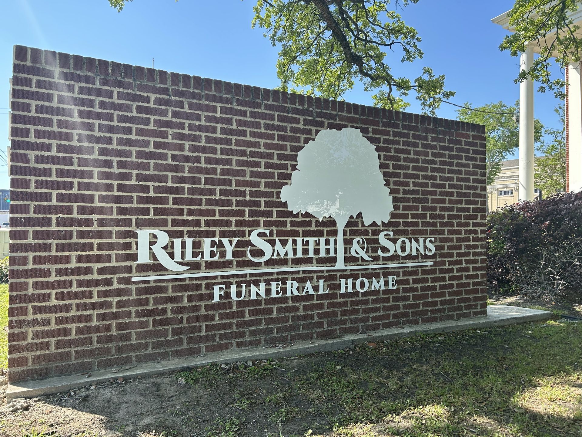 Brick sign for Riley Smith & Sons Funeral Home with white lettering and tree silhouette.