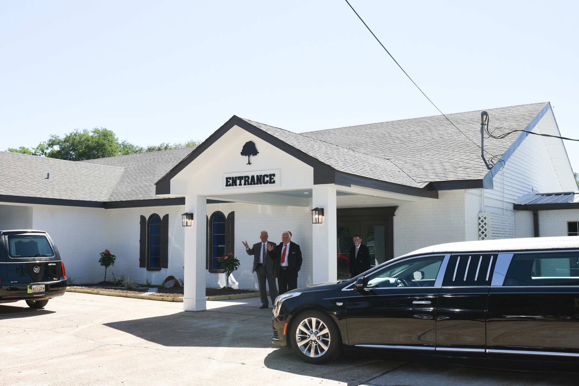 People standing outside a white building with a black car parked in front