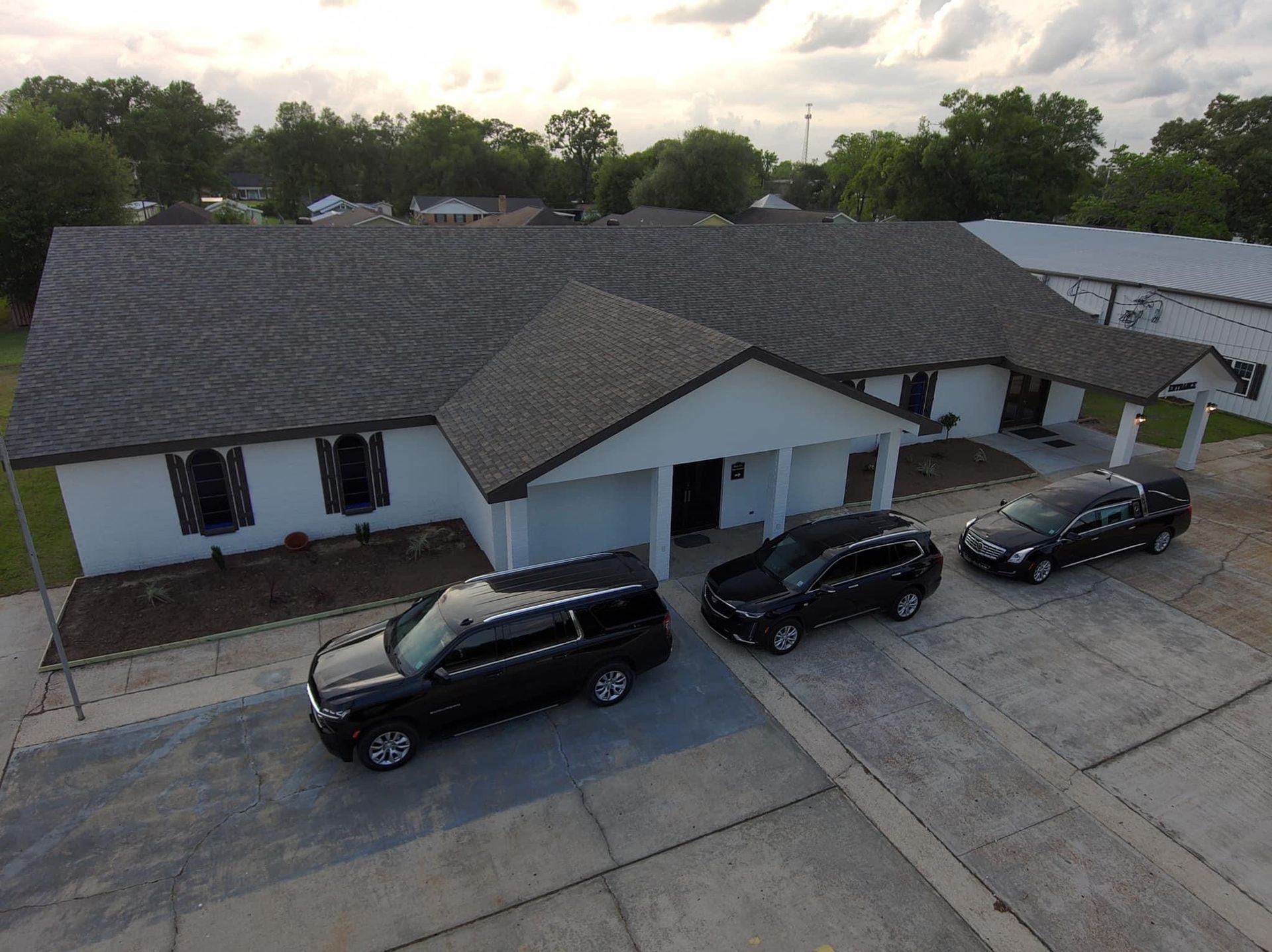 Aerial view of a white house with a dark roof and three black vehicles parked in the driveway.