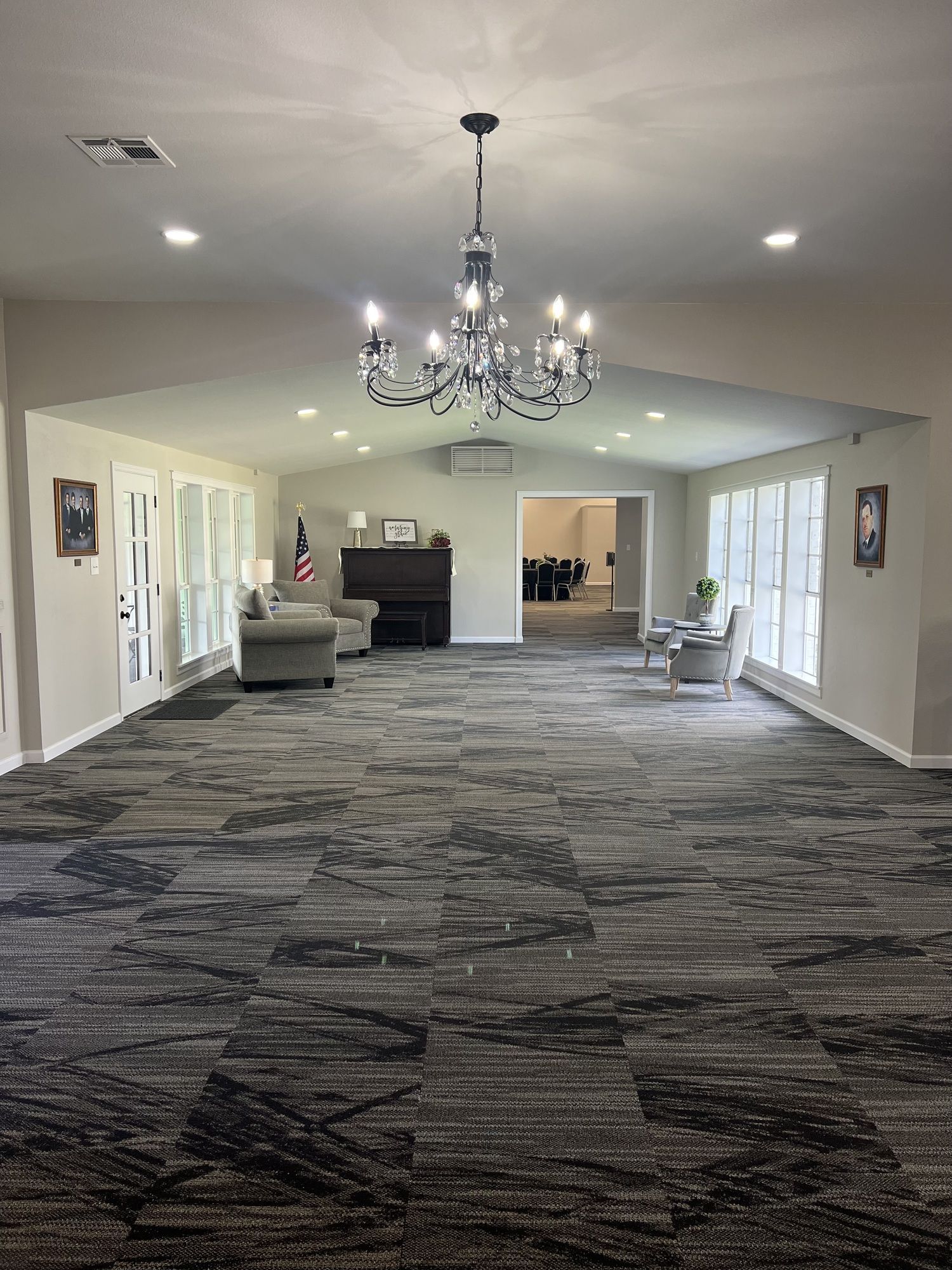 Spacious carpeted room with a chandelier, recessed lights, and seating along the walls.