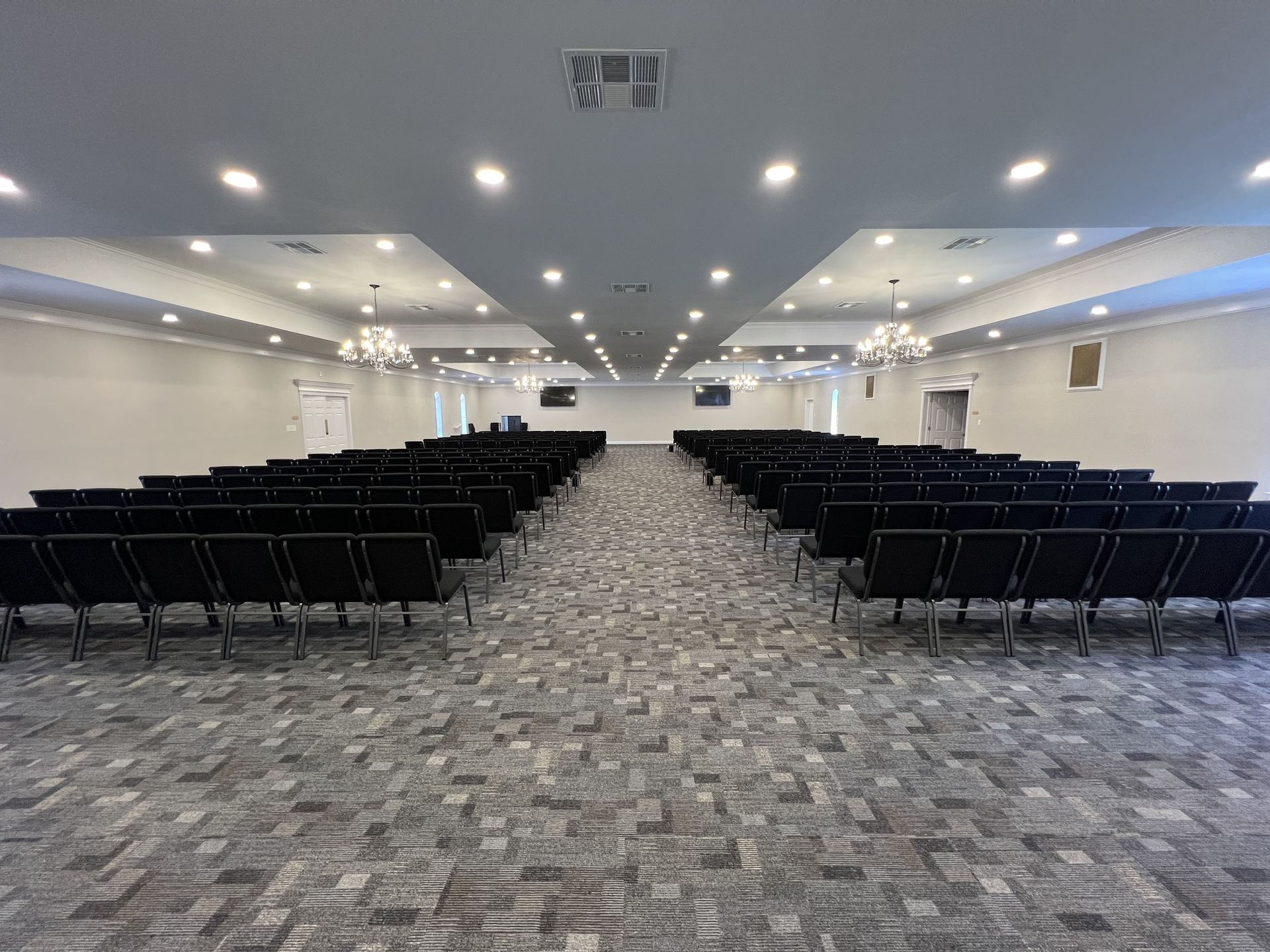 Empty conference hall with rows of black chairs and carpeted aisle under bright ceiling lights