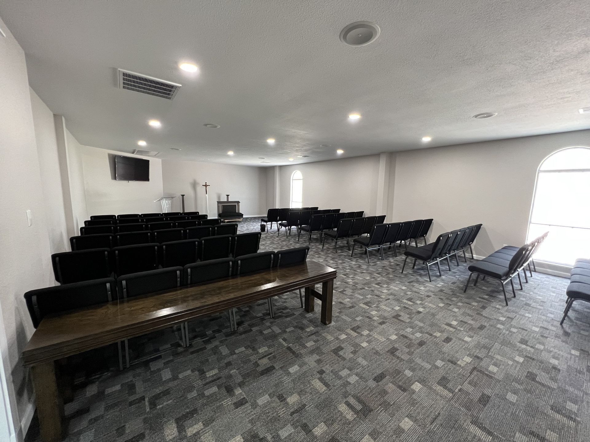 Empty conference room with rows of black chairs, a long wooden table, and bright ceiling lights