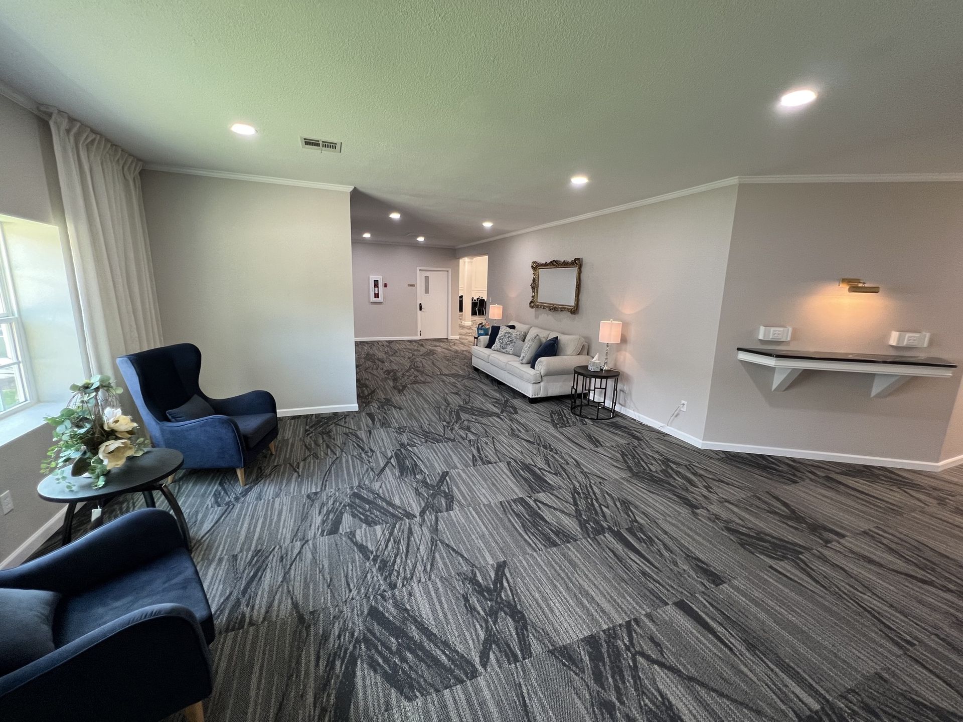 Bright modern living room with gray patterned carpet, white walls, blue chairs, and a sofa with lamp.