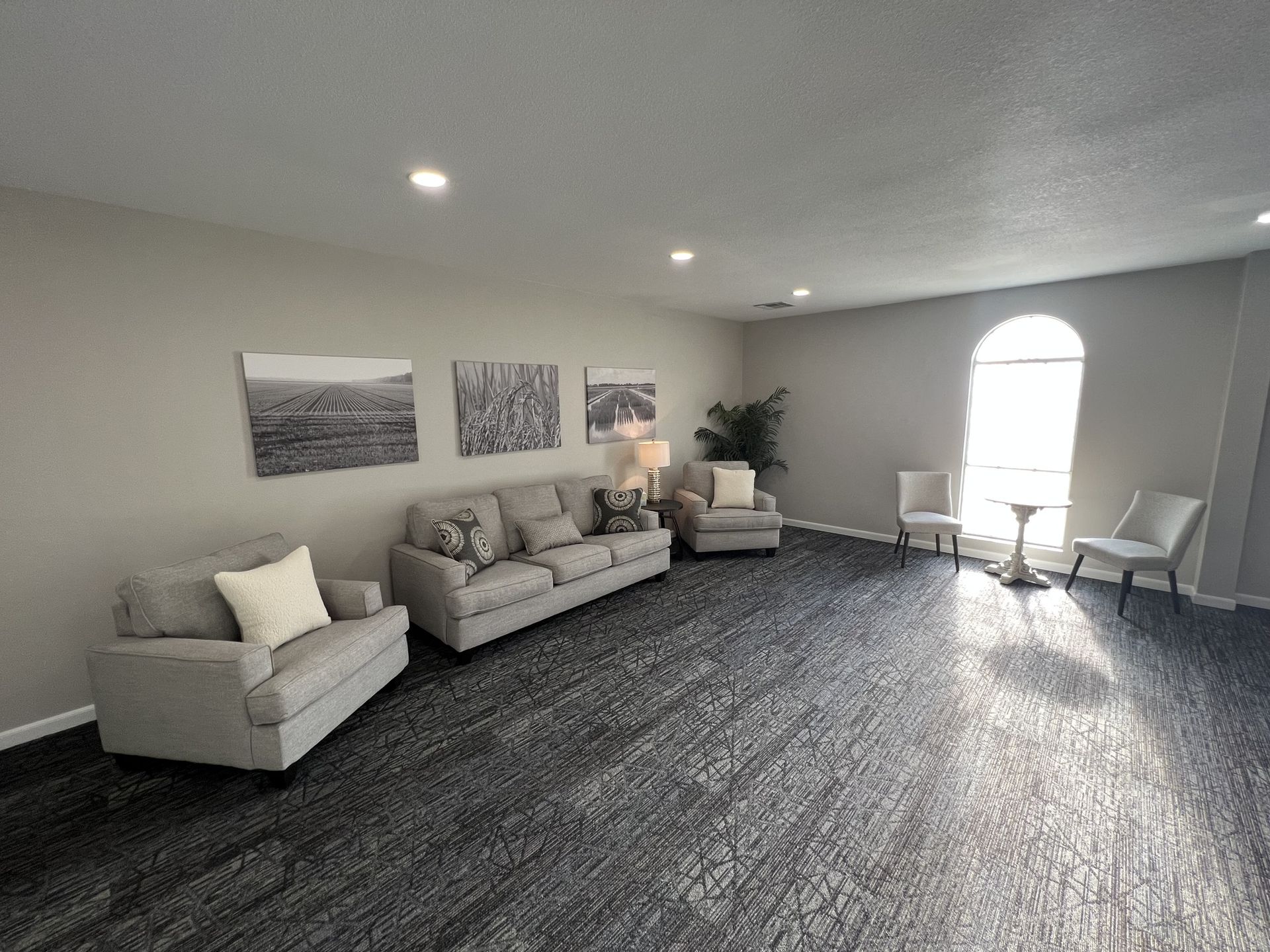 Bright modern living room with gray sofas, wall art, chairs, and an arched window.