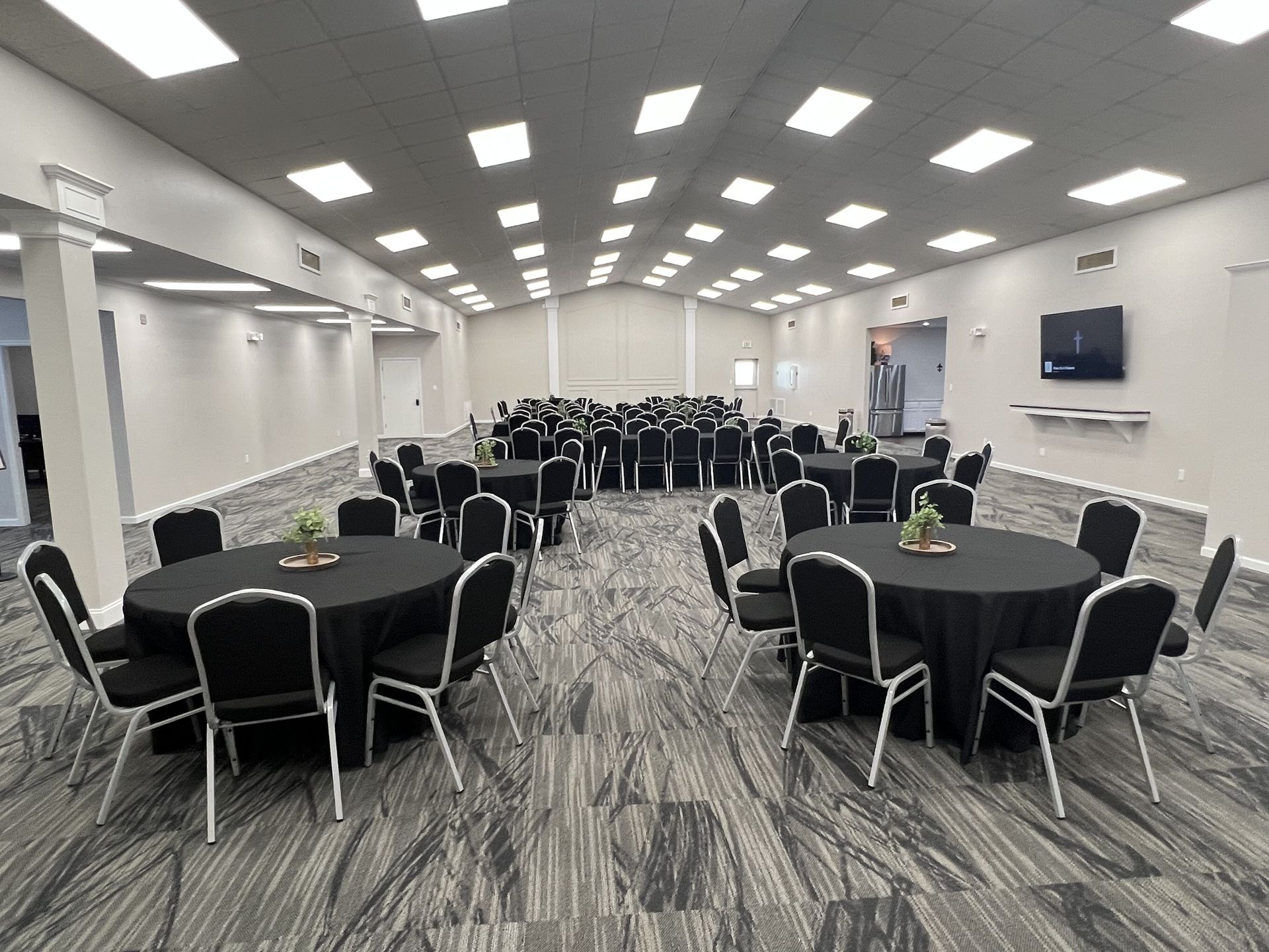 Conference room with round black tables, black chairs, and bright ceiling lights on a patterned carpet.