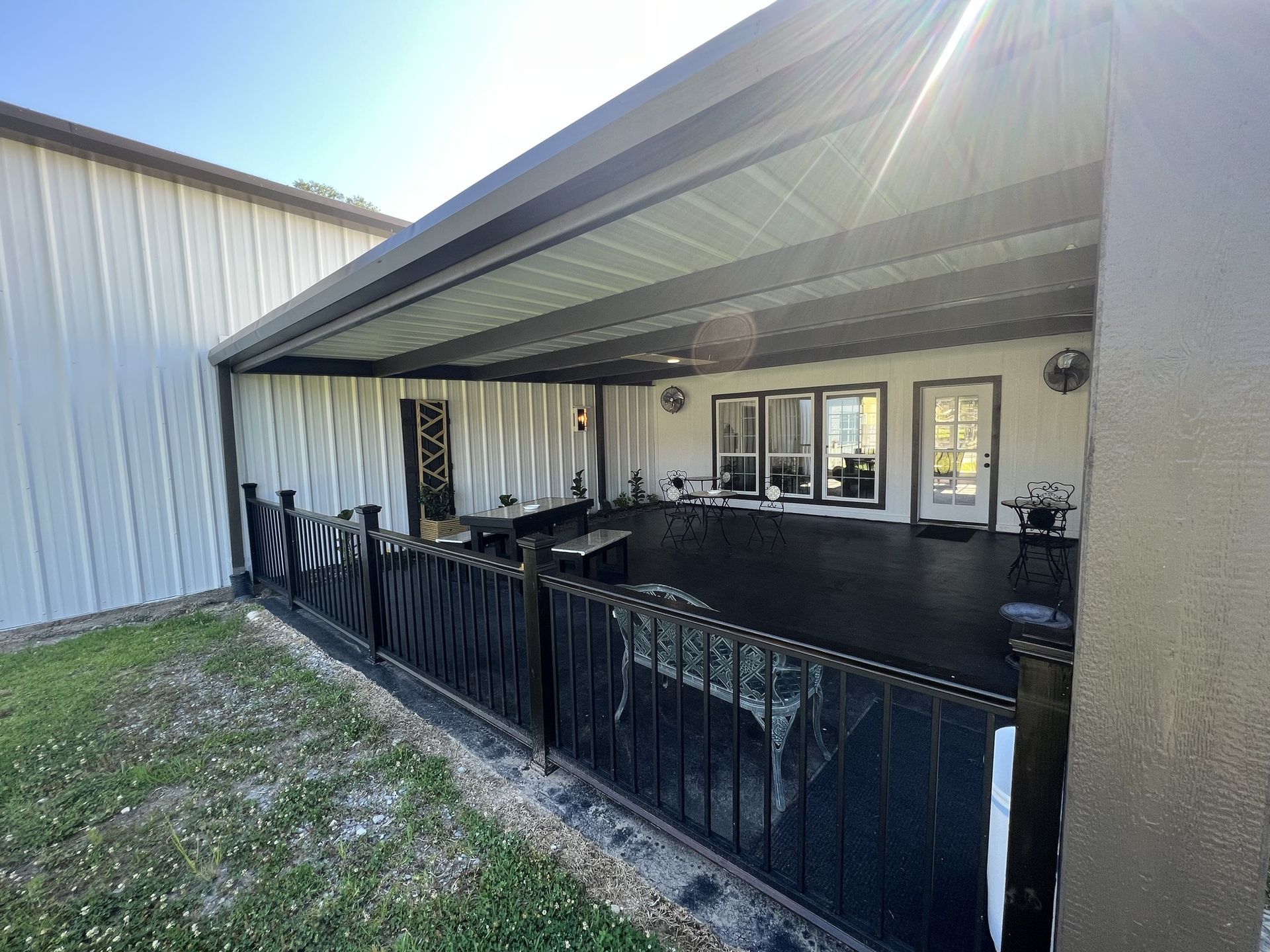 Covered porch with black railing, patio furniture, and sliding glass doors on a beige house.