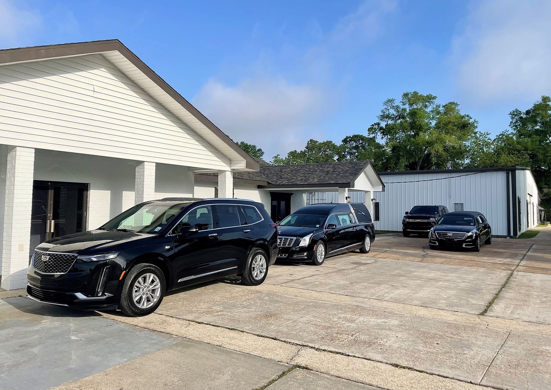 Three black cars parked outside a white building on a gravel lot under a blue sky