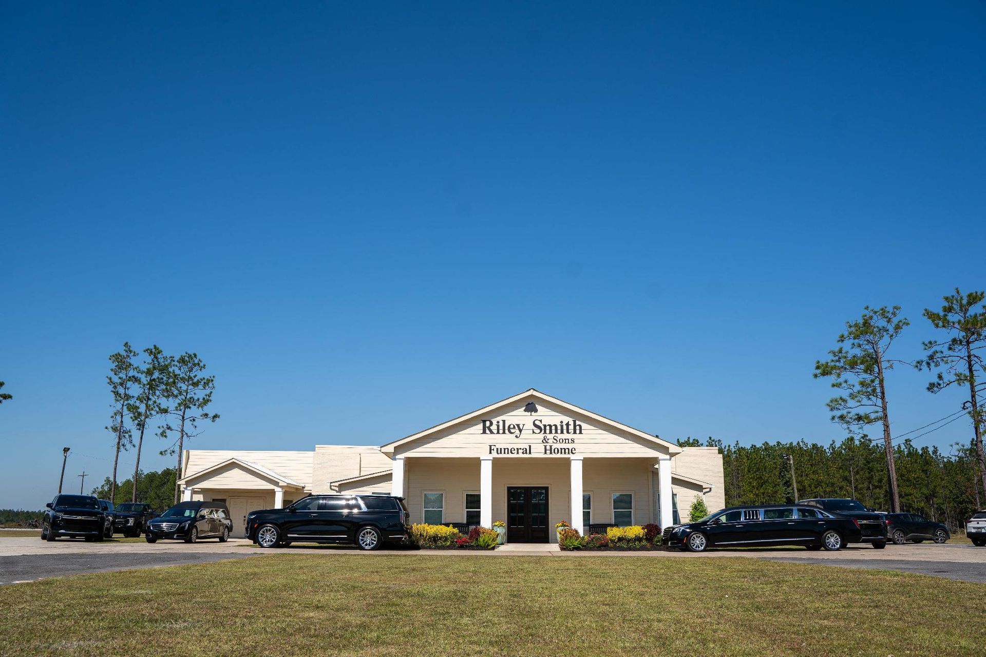 Front view of a beige church building with parked cars under a clear blue sky